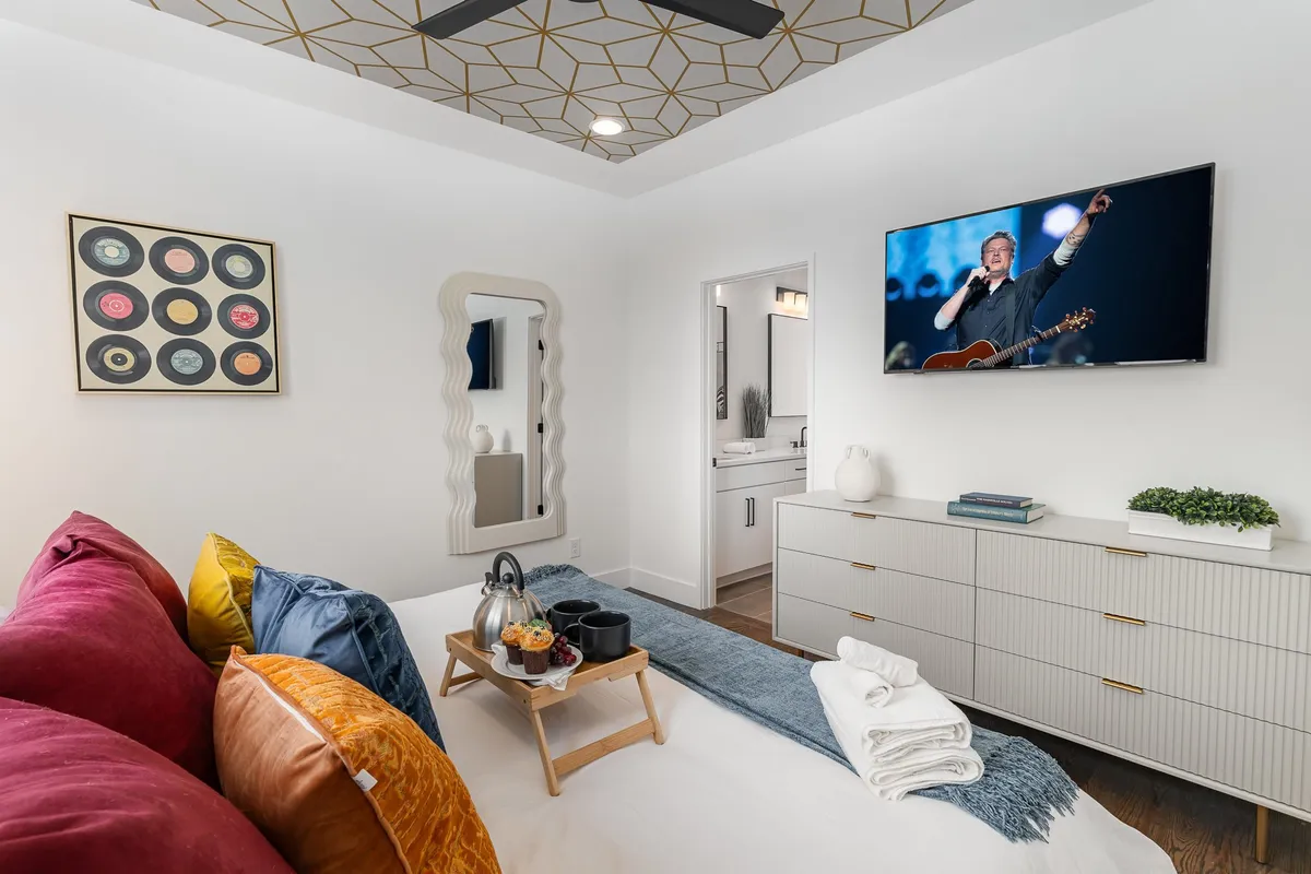 A stylish, comfortable interior living space with colorful throw pillows, modern décor, and a television displaying a live performance. The room feels vibrant yet relaxing, perfect for unwinding after a night out or gathering with friends to enjoy music together.