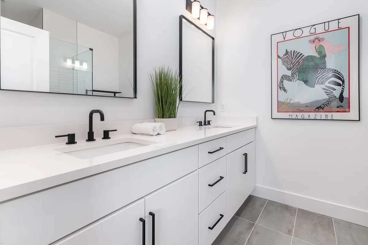 A stylish bathroom with dual sinks, large mirrors, a Vogue poster, towels, and a potted plant. The room feels chic and functional, ideal for morning routines or evening wind-downs.