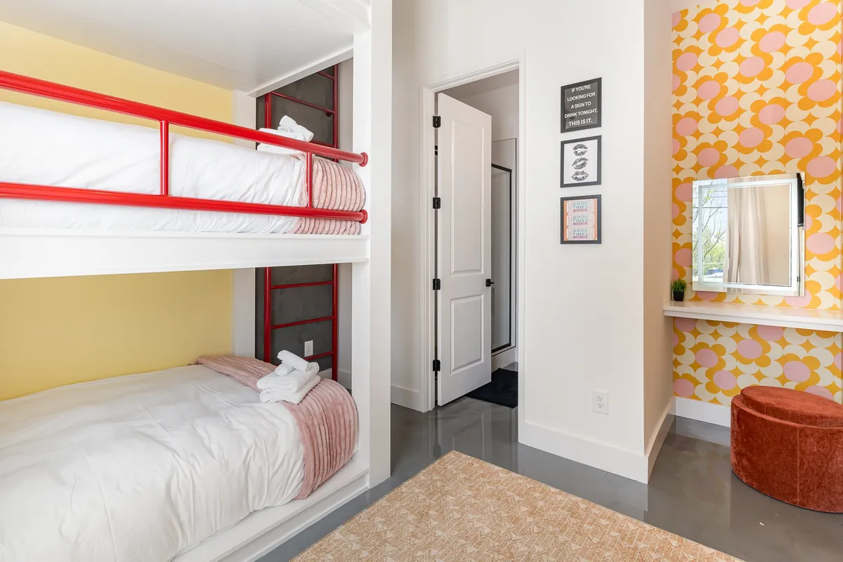 A vibrant bunk room featuring bunk beds, playful colorful wallpaper, and a dedicated vanity area. The space is energetic and ideal for group stays or kids, offering both shared sleep space and a spot to get ready.